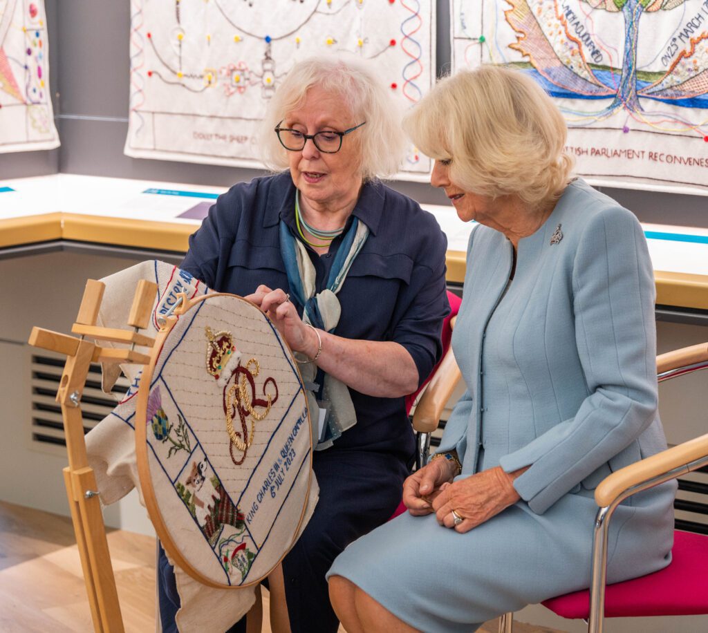 Dorie Wilkie, Head Stitcher, and Her Majesty, Queen Camilla put a stitch in a specially designed panel to mark the visit to the Great Tapestry by Their Majesties