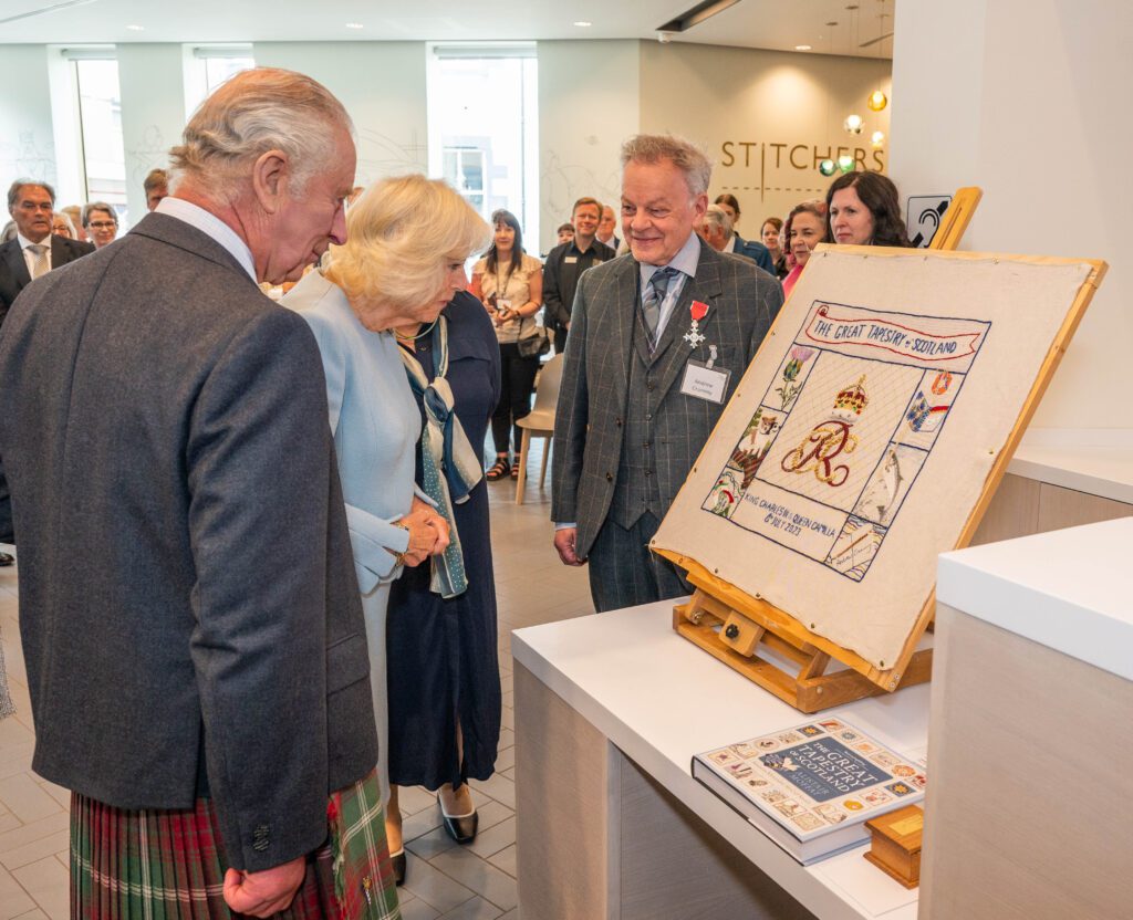 Their Majesties view the specially designed Panel to mark their visit alongside Andrew Crummy, the artist, and Dorie Wilkie, the Head Stitcher